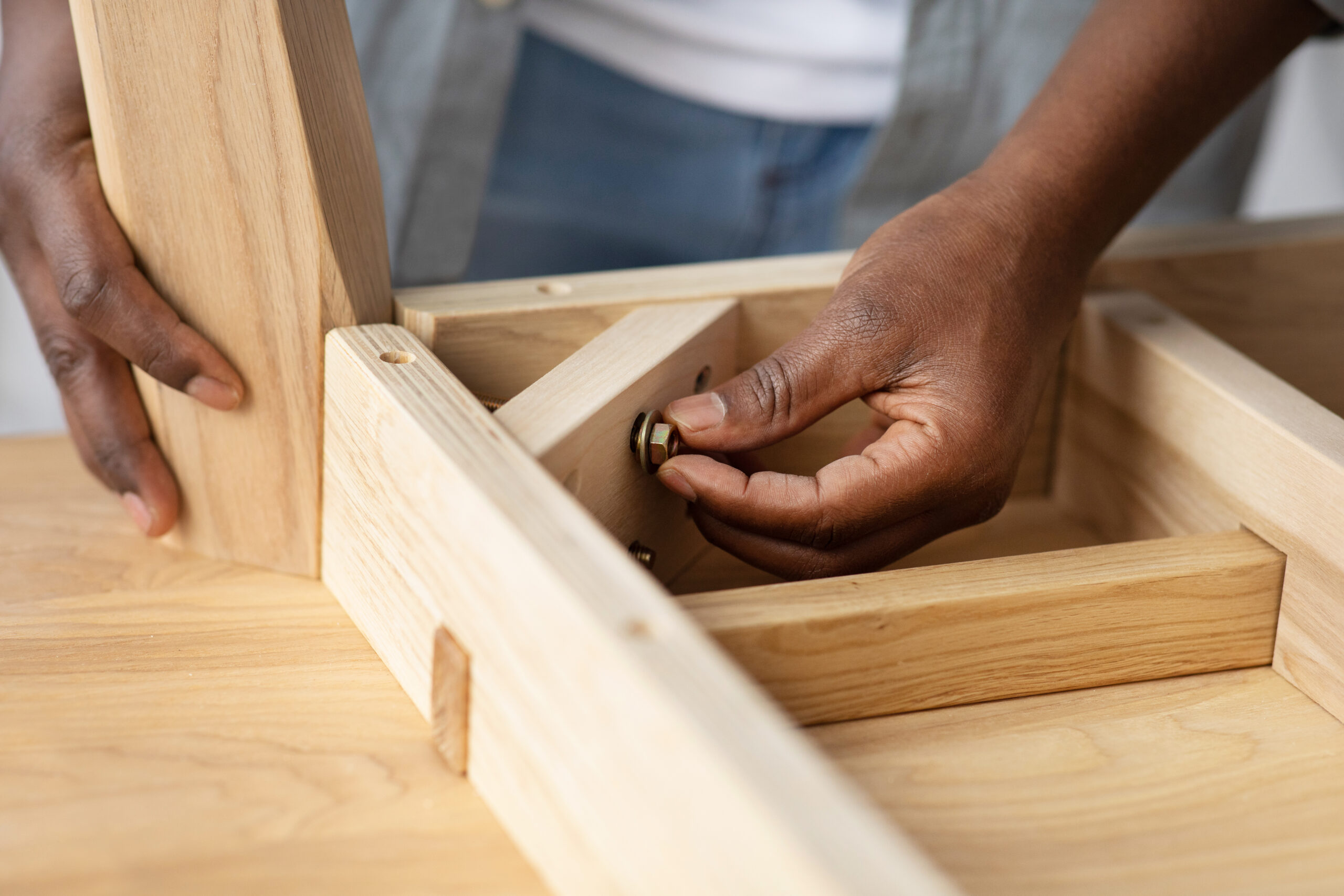 Self-assembly furniture concept. Black man screwing bolt to wooden table, installing desk by yourself at home, closeup