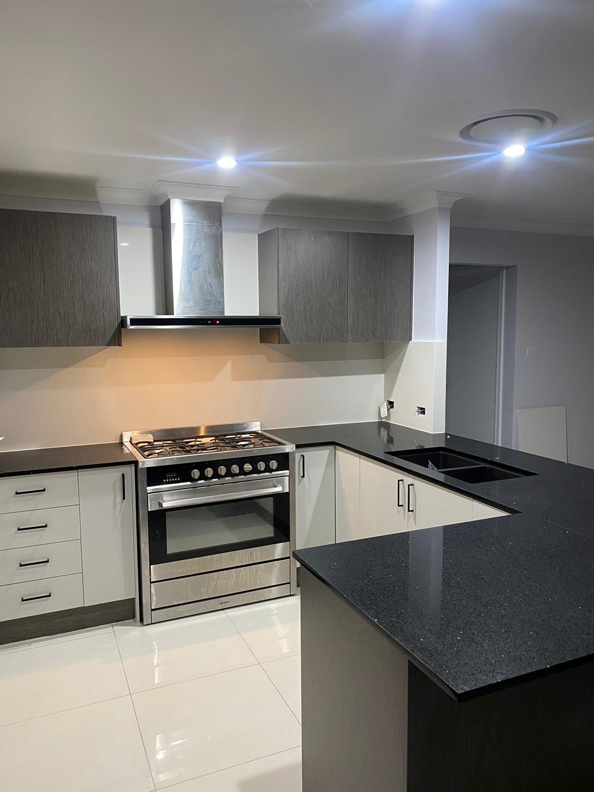 Finished kitchen with stainless steel rangehood and dark benchtops – Diagrid Constructions